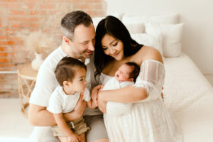 Newborn Photographer, Mom, dad and toddler son admire newborn baby in mother's arms