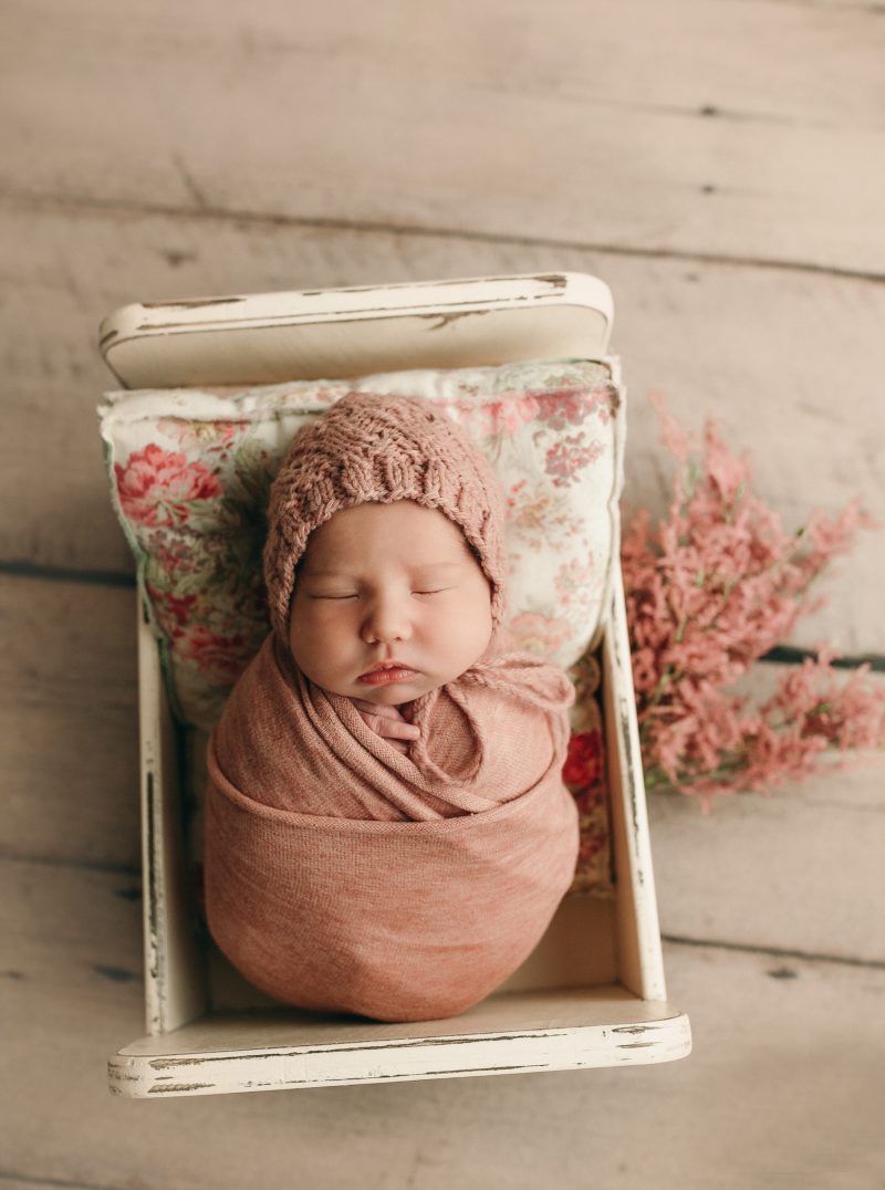 baby girl in newborn bed with pillows and florals