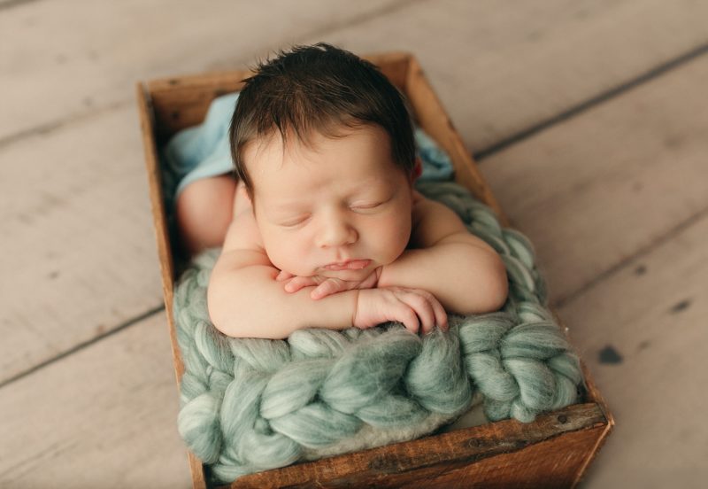 baby boy in crate with teal blanket