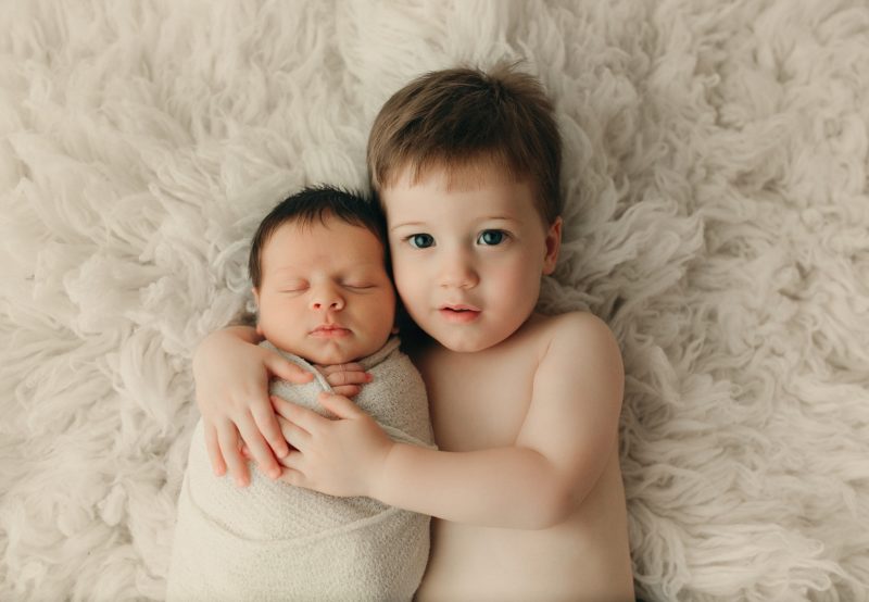 newborn baby boy with toddler sibling on white blanket
