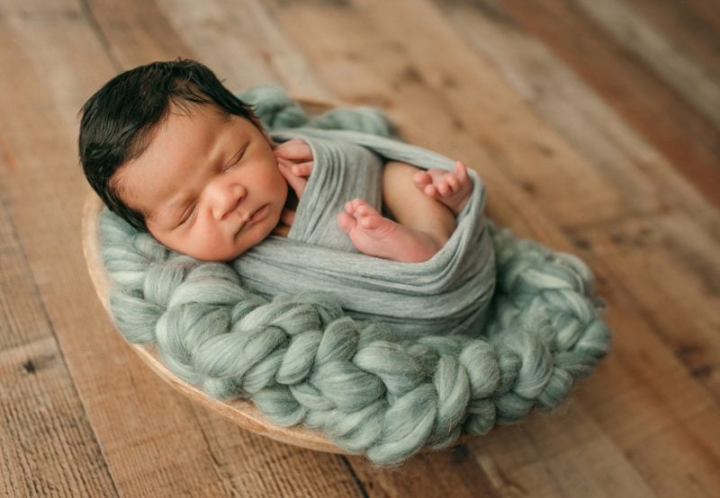 newborn boy swaddled in mint wrap on wood floor 