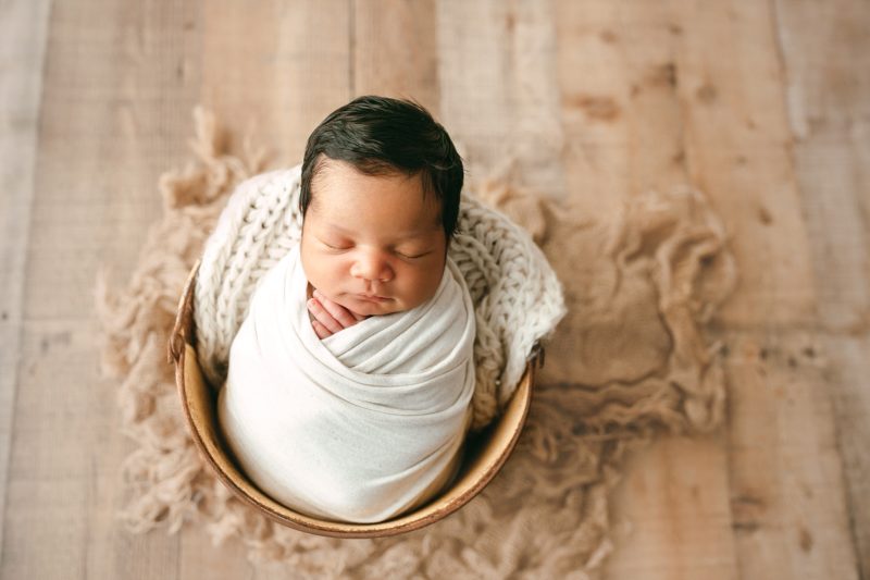 newborn boy swaddled in white in bucket