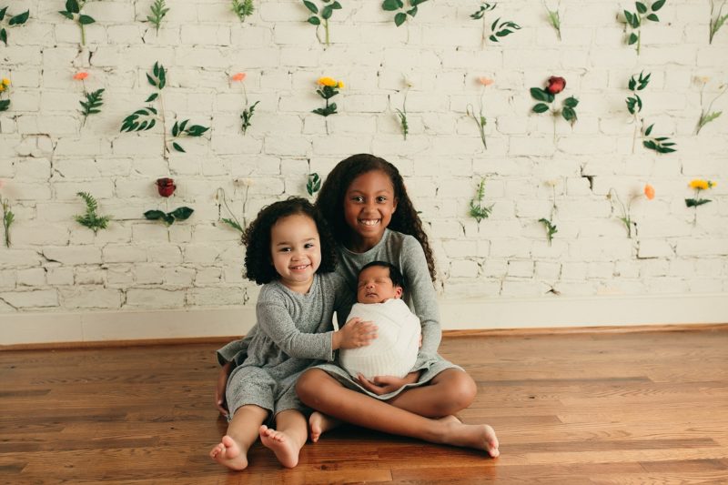 sisters holding newborn brother floral backdrop