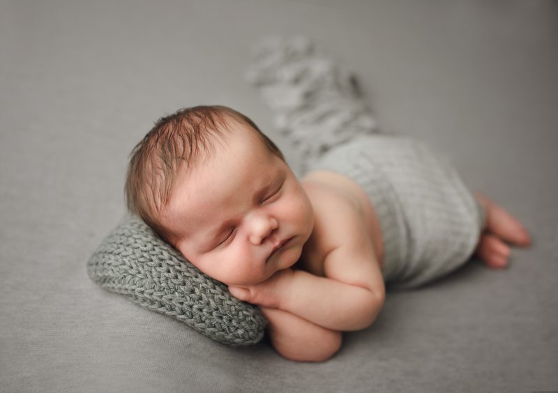 newborn boy sleeping on hands with gray pillow, mckinney newborn photographer
