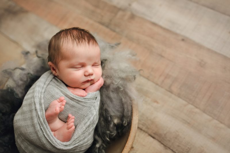 newborn boy in bowl with fur on wood floor, mckinney newborn photographer