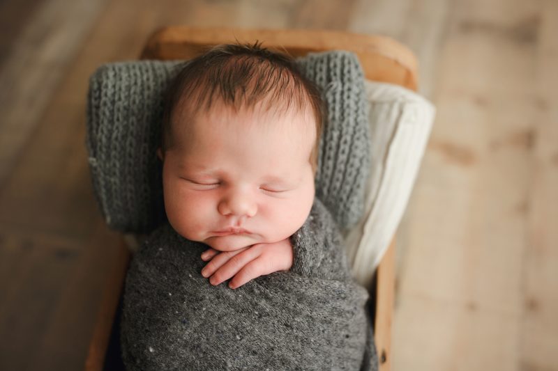 newborn boy sleeping in baby bed with gray pillow, mckinney newborn photographer