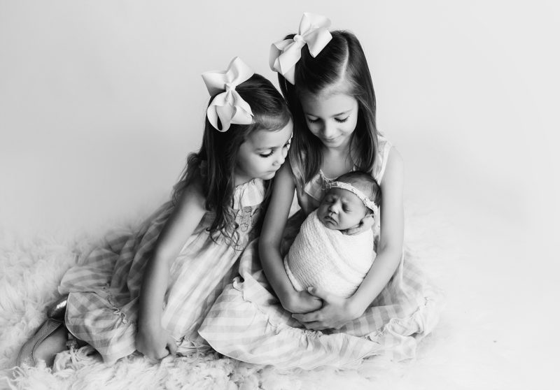 newborn swaddled with older sisters holding, mckinney newborn photographer