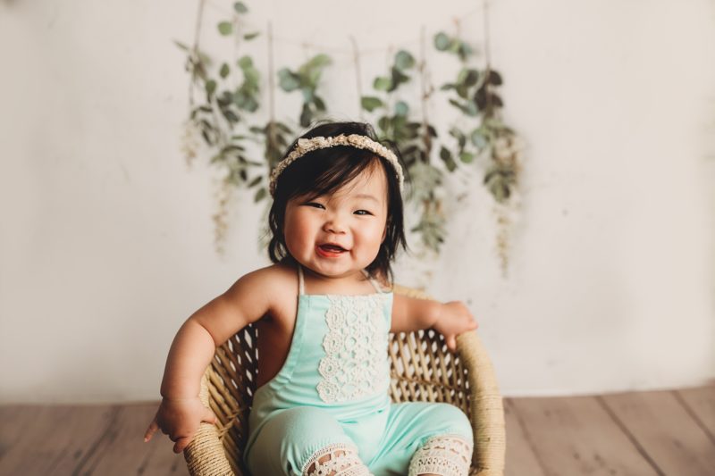 baby one year old in mint sitting on wicker chair