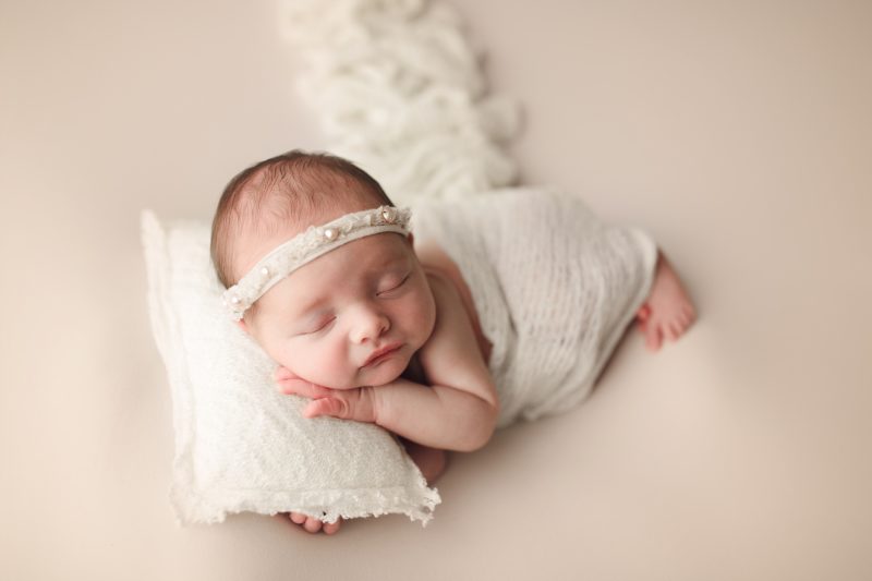 newborn swaddled in white laying on white pillow