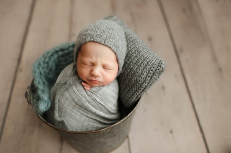 newborn swaddled in gray in metal bucket
