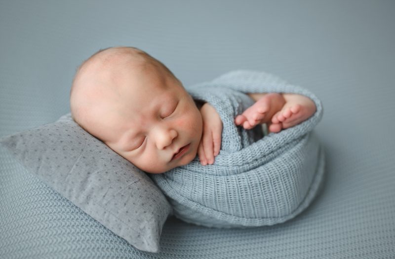 newborn boy swaddled in blue on blue blanket and gray pillow