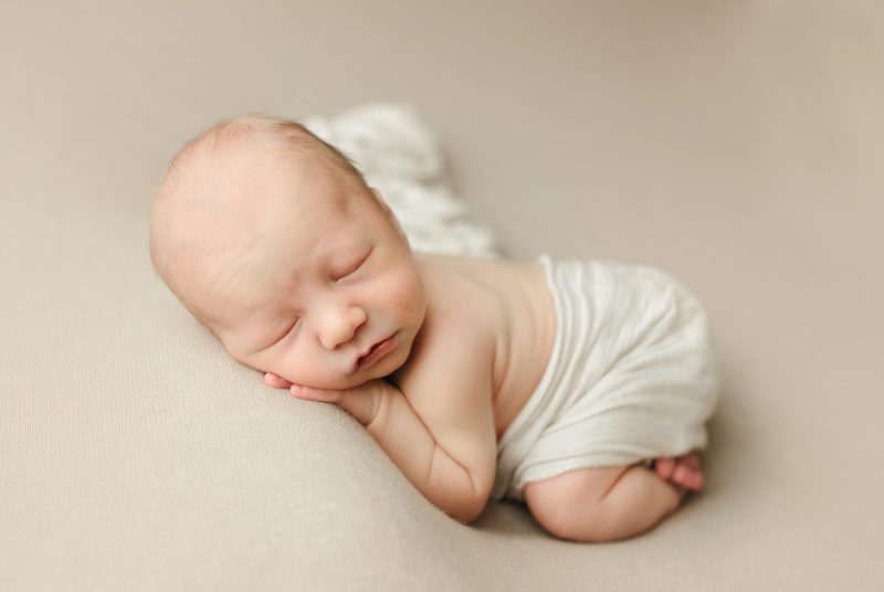 newborn boy on cream blanket sleeping on hand