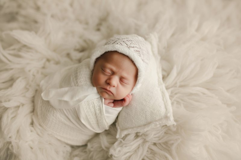 newborn girl swaddled in white on white pillow and white blanket