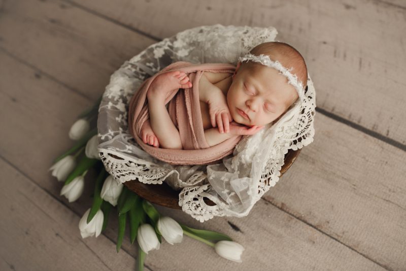 newborn swaddled in pink laying on lace with florals