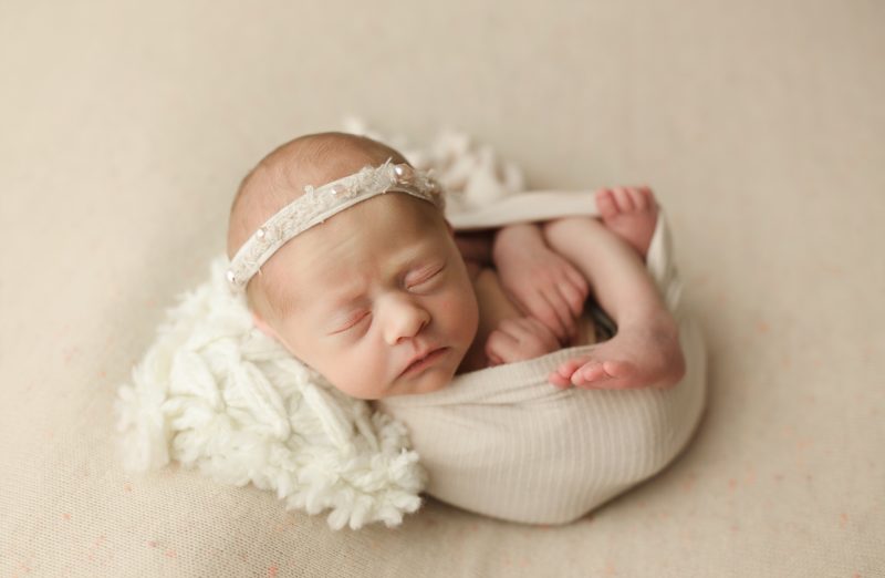 newborn swaddled in white on cream blanket