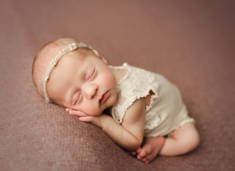 newborn wearing cream outfit sleeping on hands on pink blanket, dallas newborn photos baby zoe