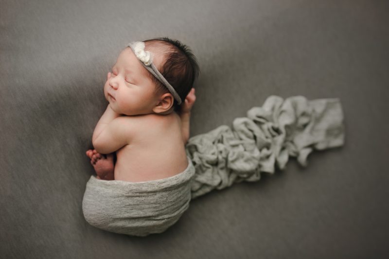 newborn laying on tummy swaddled in gray on gray blanket