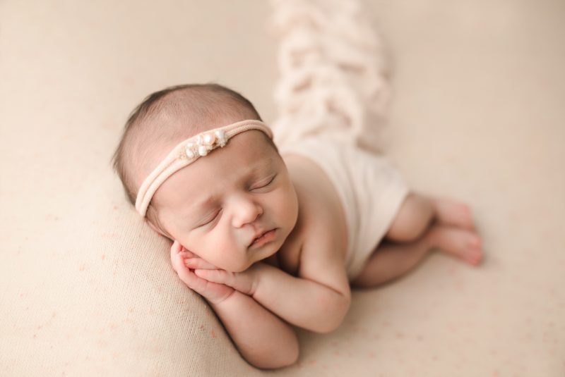 newborn swaddled in cream on cream blanket laying on hands