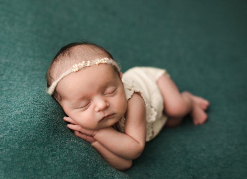 newborn girl in cream outfit on green blanket