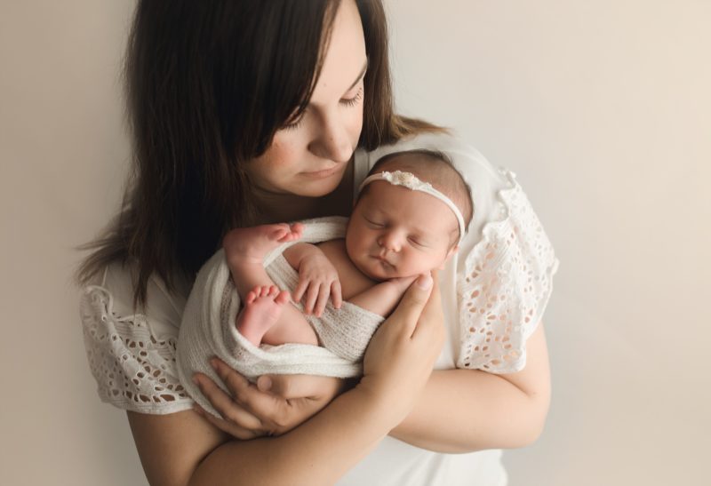 newborn portrait mom holding baby girl on white wall