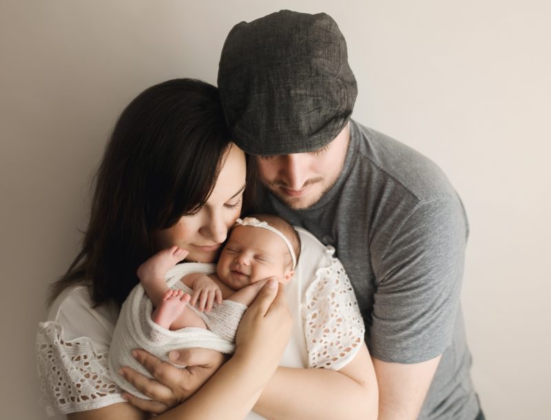 newborn portrait with mom and dad holding baby on white wall