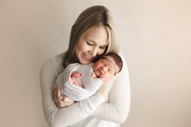 mom holding swaddled newborn girl wearing white