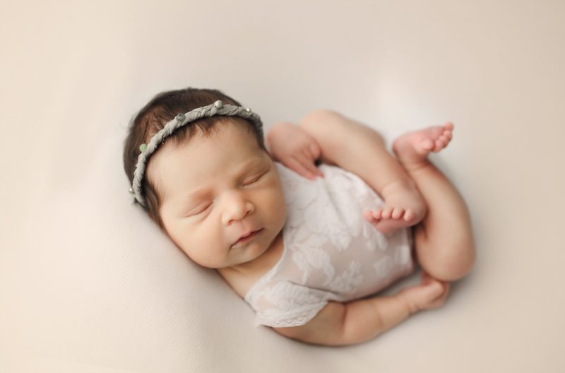 newborn girl with legs crossed sleeping on cream blanket