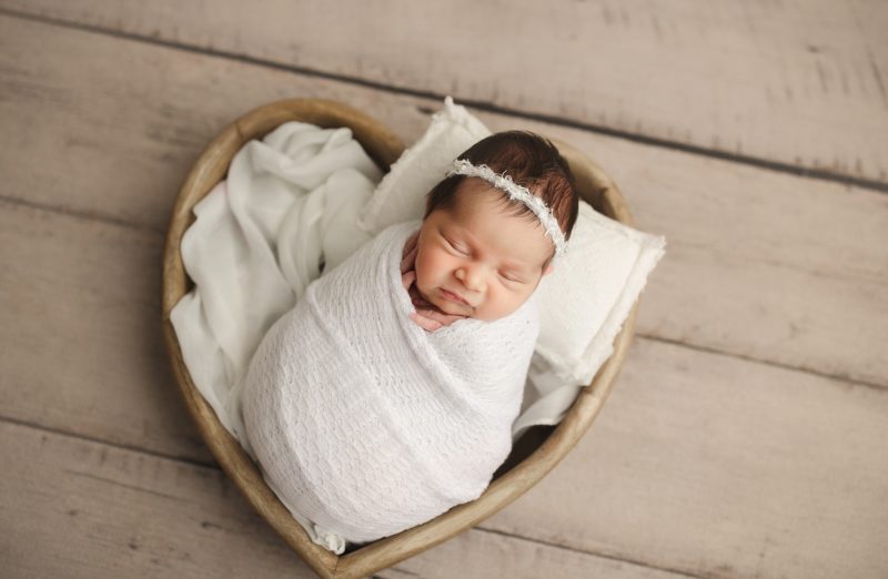 newborn swaddled in white in heart shaped basket