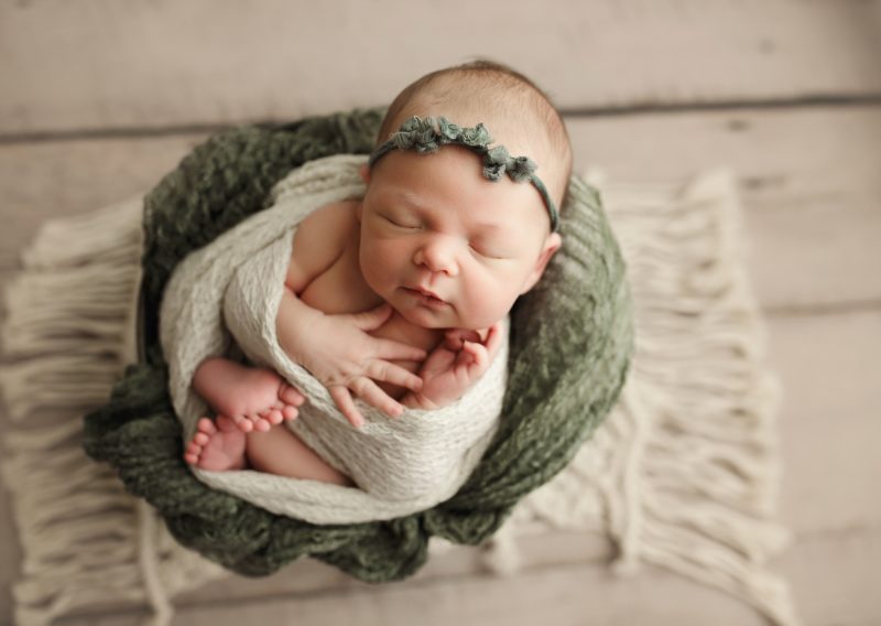 baby swaddled in basket with green blanket and headband