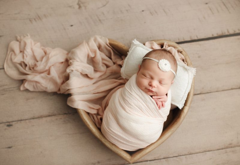 newborn swaddled in pink in heart shaped basket