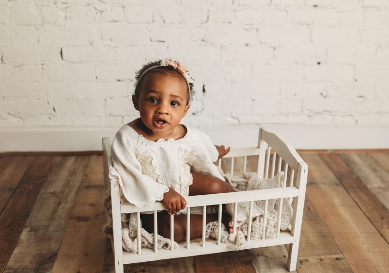 baby sitting up in mini crib white brick background, baby mini sessions mckinney baby photographer