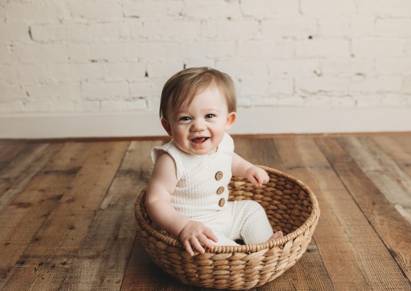 baby sitting up in cream romper in basket, baby mini sessions mckinney baby photographer