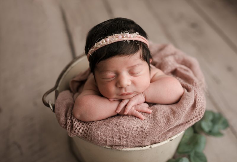 newborn in bucket with head on hands
