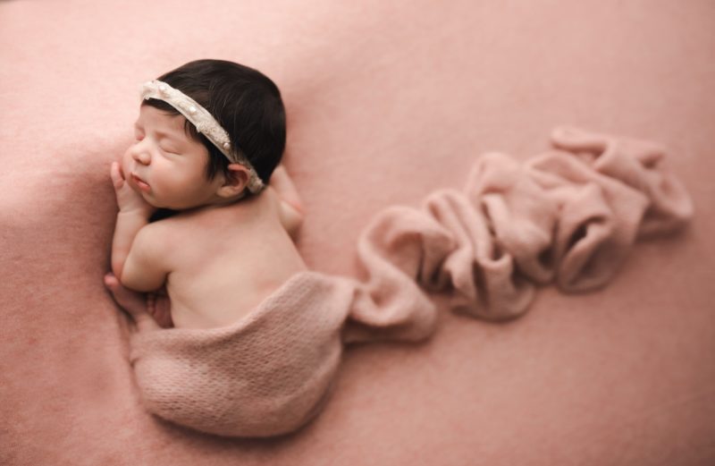newborn laying on pink blanket with swaddle