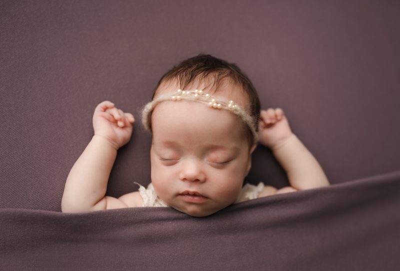 newborn laying on back with arms up on purple blanket, newborn photo session mckinney texas