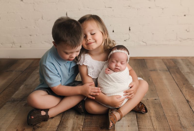 older siblings holding swaddled newborn