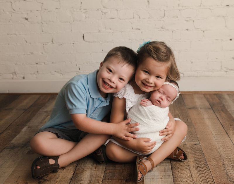 newborn portrait with older siblings holding swaddled baby
