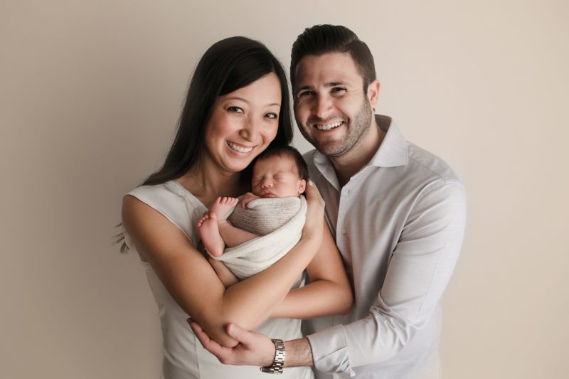 newborn family portrait mom and dad on cream backdrop