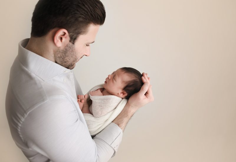 newborn portrait dad holding baby with cream backdrop