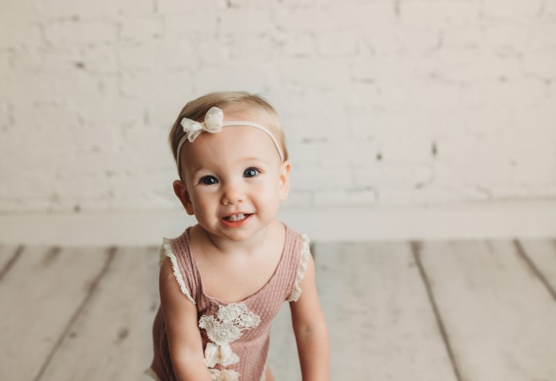 baby smiling in mauve romper on white brick wall, mckinney baby photo session baby charlie