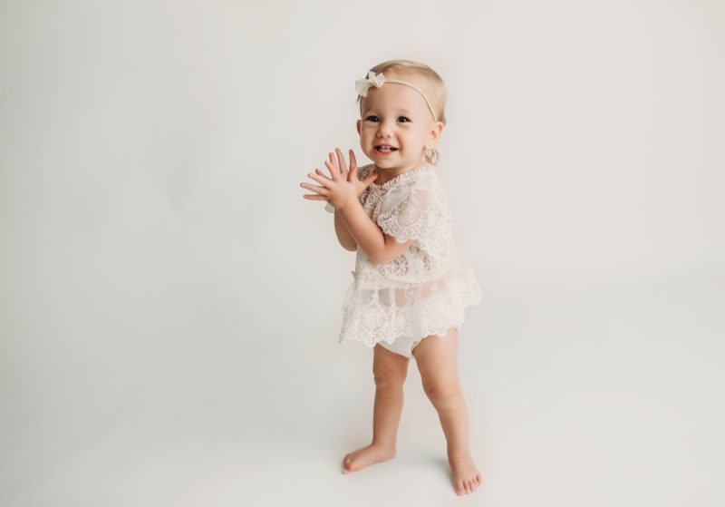 baby standing clapping hands on white backdrop