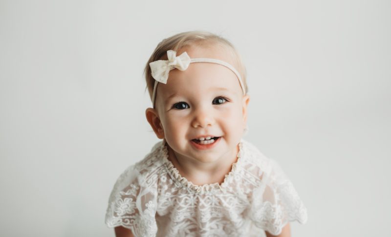baby smiling in white outfit on white backdrop