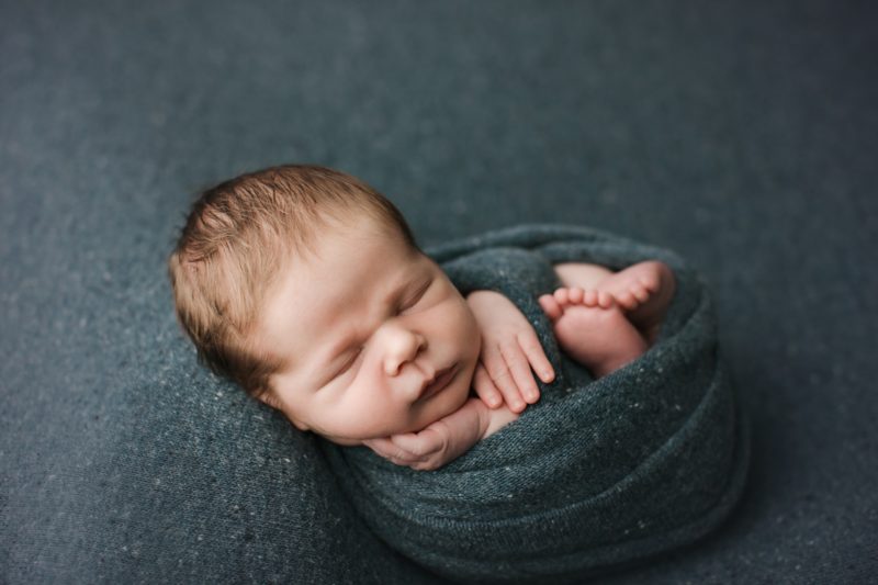 newborn swaddled in green sleeping on green blanket
