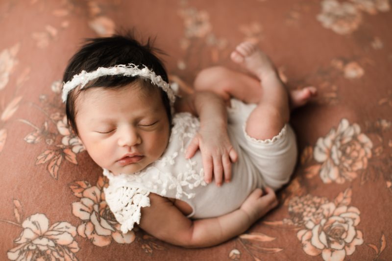 newborn girl wearing white romper on floral blanket_dallas baby photo session baby leia