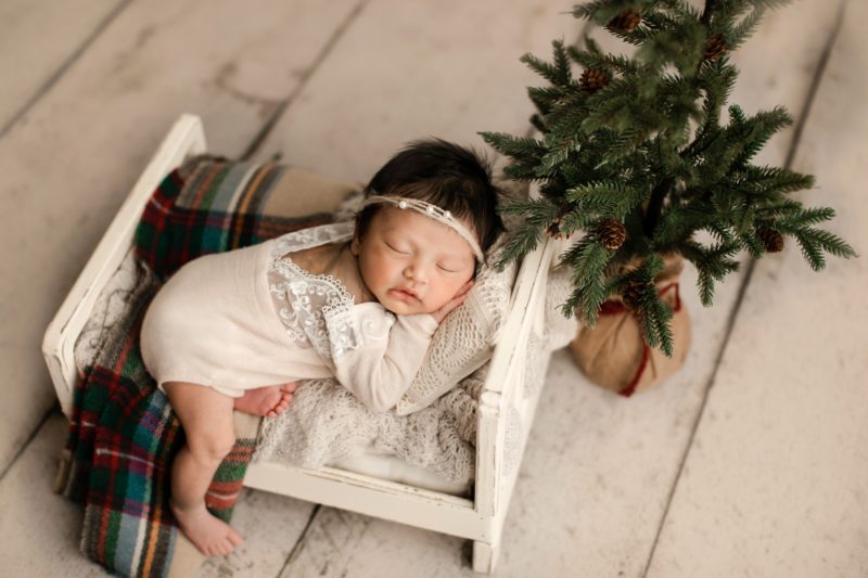 newborn girl laying on baby bed with christmas tree