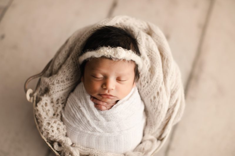 newborn girl swaddled in white white floor background