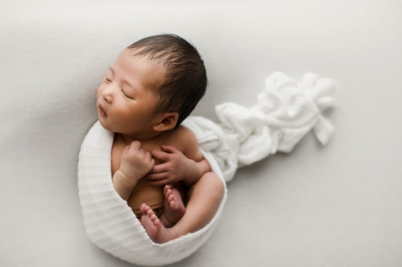 newborn boy swaddled in white laying on back on white blanket_mckinney baby photo session baby alex