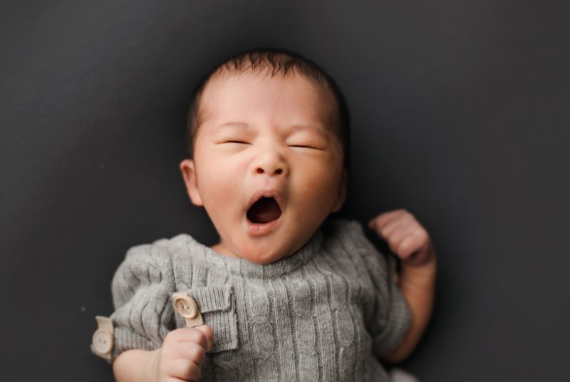 newborn boy yawning in gray outfit